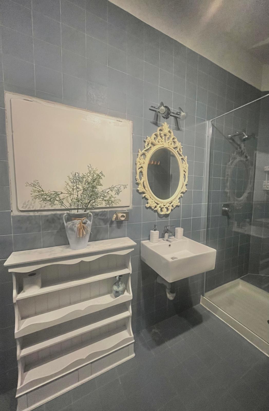 Bagno con piastrelle grigie, doccia e specchio decorato